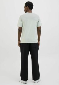 Lichtgroene katoenen t-shirt met korte mouwen, gecombineerd met losse zwarte broek met zakdetails. Witte sportschoenen maken de look af.