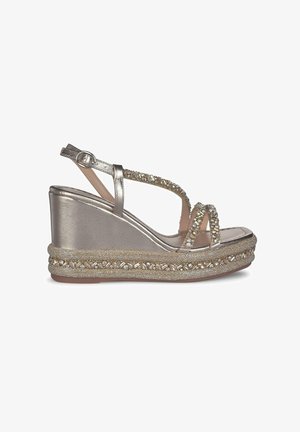 Sandalias de cuña con tiras metálicas plateadas, adornadas con strass. Presentan una base texturada y trenzada con un acabado brillante. Cierre de hebilla.