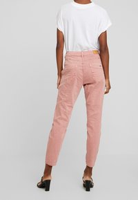 Rosa, avsmalnande byxor med en skrynklig textur och bakfickor. Bärs med en vit kortärmad skjorta och svarta klacksandaler.