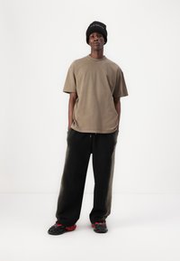 Hnědé oversized tričko a černé tepláky; červené a černé tenisky; textilie vypadá měkce; černá čepice s nápisem.