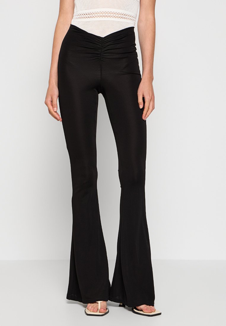 Pantalones negros de campana con una textura suave, que presentan un detalle fruncido en la cintura. Están hechos de un material elástico para mayor comodidad y ajuste.