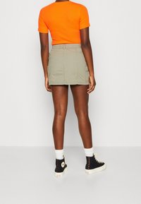 Oranžový top s krátkým rukávem ve spojení s khaki džínovou sukní s bočními kapsami a černými vysokými teniskami s bílou podrážkou a červenými akcenty.