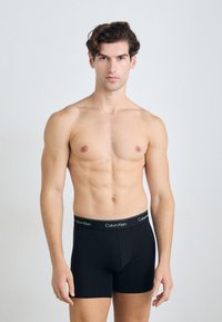 Fekete pamut boxer alsónadrág, testhez simuló szabással és rugalmas derékpánttal, amelyen a Calvin Klein logó fehér színben látható. Sima tapintású, minimalista stílusú.