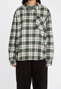 Chemise en flanelle à carreaux verts et blancs avec une fermeture à boutons, une poche poitrine et des manches longues. Matériau texturé avec des motifs à carreaux contrastés.