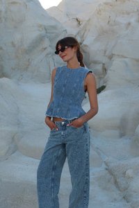Denim-toppi, jossa on peplum-helma ja hihattomuus, yhdistettynä leveälahkeisiin denim-housuihin, molemmat huokoista vaaleansinistä kangasta.