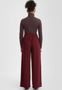 Długie bordowe spodnie o szerokich nogawkach i elastycznym pasie w połączeniu z przylegającym ciemnym golfem. Gładka tkanina, minimalna faktura.