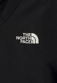 Tissu noir avec logo et texte The North Face brodés en blanc sur la zone de la poitrine d'un vêtement.