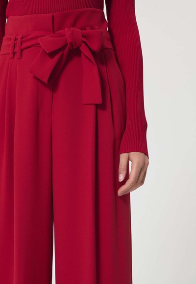 Pantalon large rouge taille haute avec ceinture en tissu nouée en nœud, porté avec un haut rouge à manches longues côtelé.