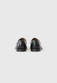 Zwarte leren schoenen met een gladde afwerking, voorzien van een lage hak, stiksels en een open achterkant ontwerp.