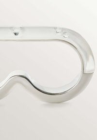 Gafas de acrílico transparente con un diseño liso y curvado. Presenta sutiles gotas de agua a lo largo del armazón. Los acentos plateados realzan el acabado brillante.