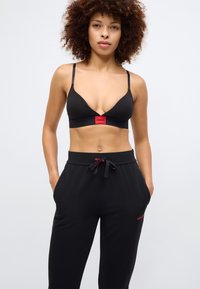 Black bralette with thin straps and red logo detail at center, paired with black sweatpants featuring red logo near waistband and pockets.