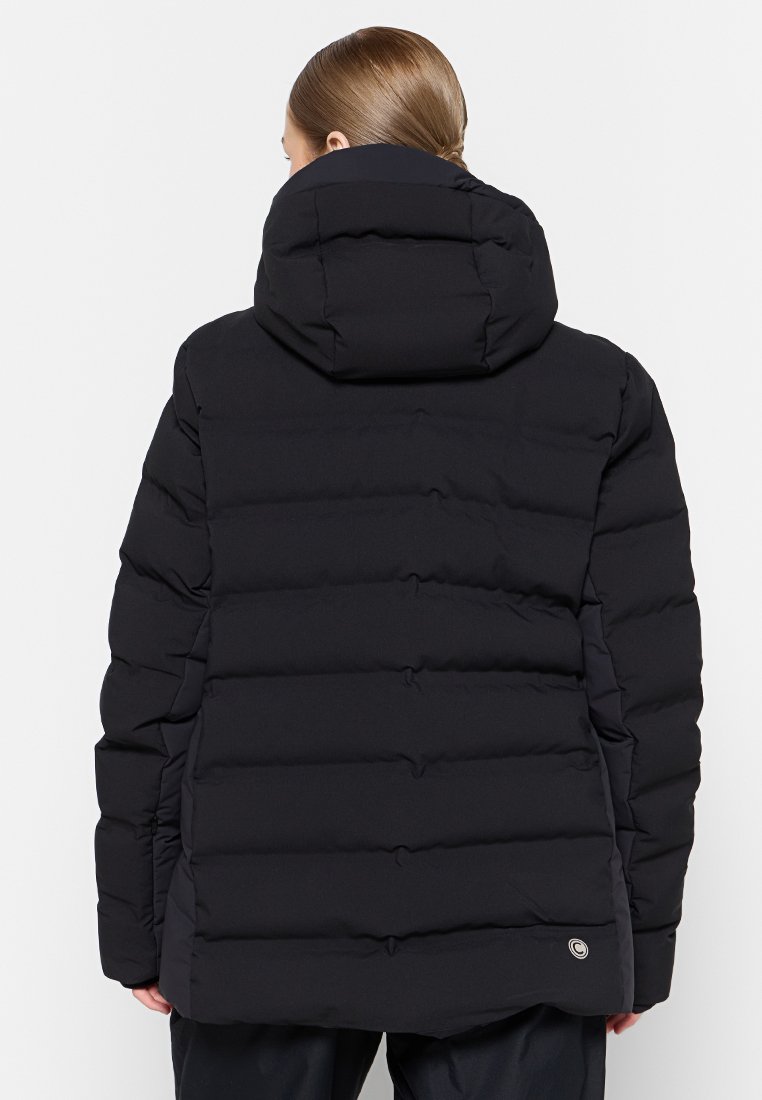 Donna con capelli castano chiaro raccolti in una treccia, indossa un giubbotto invernale imbottito nero con cappuccio, vista di spalle.