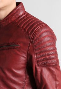 Rode leren jas met gewatteerde schouderdetails, inclusief een met rits afsluitbare zak en een zachte, rijke textuur. Hoog design van de kraag.