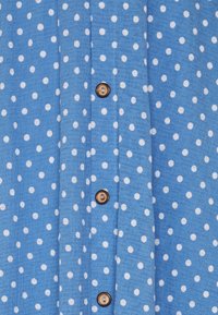 Modrá látková košile s bílými puntíky, s knoflíkovým zapínáním na hnědé knoflíky, strukturovaným povrchem a rovnými lemy.