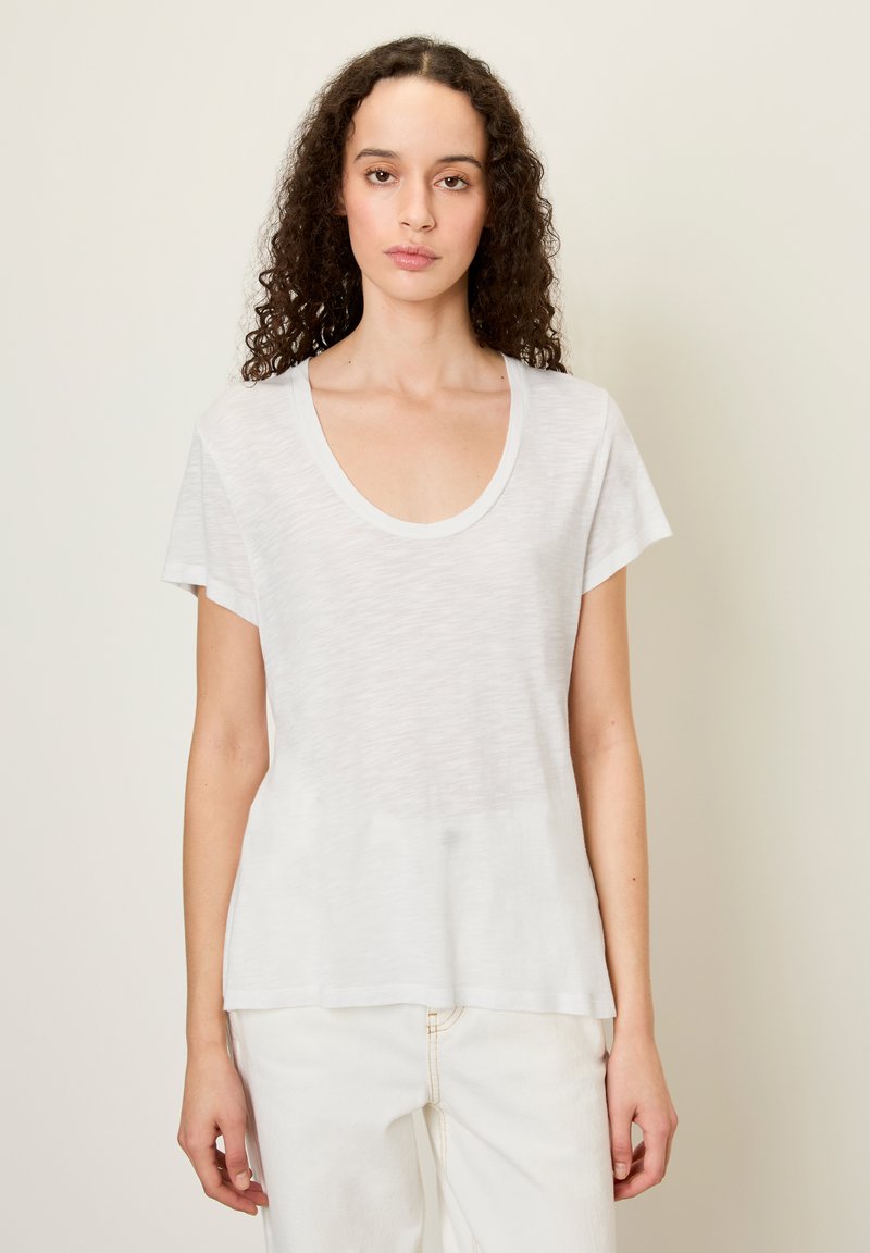 Balta trumpa mėlyna marškinėliai su plačiu apykaklės iškirpimu, pagaminti iš lengvos, struktūrinės medžiagos. Turi laisvą siluetą ir subtilų raštą.