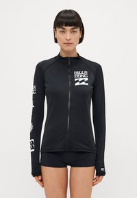 Črna rash guard majica s kapuco in dolgimi rokavi. Ima bel logo blagovne znamke in dizajne na rokavih. Narejena je iz gladkega, raztegljivega materiala.