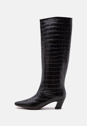 Botte noire mi-mollet avec texture crocodile, bout pointu et talon bas incliné sur fond blanc.