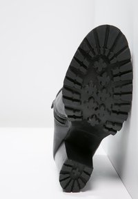 Bottine en cuir noir avec une semelle en caoutchouc texturé arborant un motif floral. Détail de fermeture éclair latérale visible sur le dessus de la bottine.