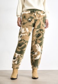 Fleecebukser med camouflage-mønster i beige, grønt og hvitt; elastisk midje med snor; avsmalnende mansjetter ved anklene.