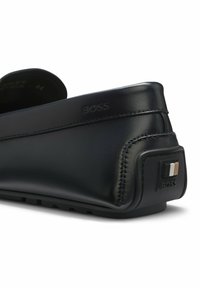 Mocassin en cuir noir avec le logo BOSS embossé sur le côté et talon en caoutchouc arborant des rayures noires, blanches et beiges.