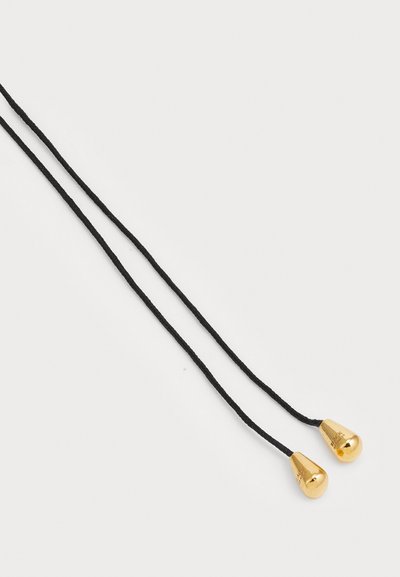 Cuerda trenzada negra con dos puntas de metal dorado en cada extremo. Las puntas tienen forma de lágrima y son brillantes, reflejando la luz.