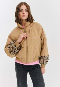 Hnedá prešívaná bunda s ružovými detailmi, vybavená pufovanými rukávmi s leopardím vzorom a skráteným strihom. Zapínanie na zips a elastické manžety.