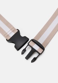 Pasek z beżowym materiałowym paskiem i białym paskiem, z czarnymi plastikowymi sprzączkami i elementami do regulacji na obu końcach.