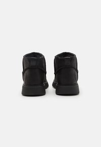 Bottines noires avec une texture en daim doux, bout rond, col rembourré et semelle en caoutchouc plate. Présente des accents de couture à l'arrière.