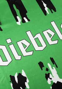 Groene stof met gedurfde, witte letters die "Diebel" spellen, met zwart-witte verfsplatterpatronen die textuur en contrast creëren.