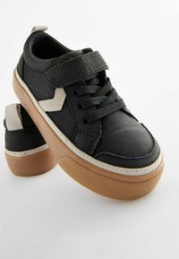 Svarta syntetiska sneakers med en beige gummisula, utrustade med en kardborreband, svarta snören och en strukturerad beige detalj.