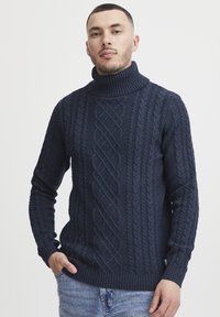 Pull en col roulé en maille bleu marine avec un motif en torsades, des poignets et un ourlet côtelés. Texture douce et coupe ajustée.