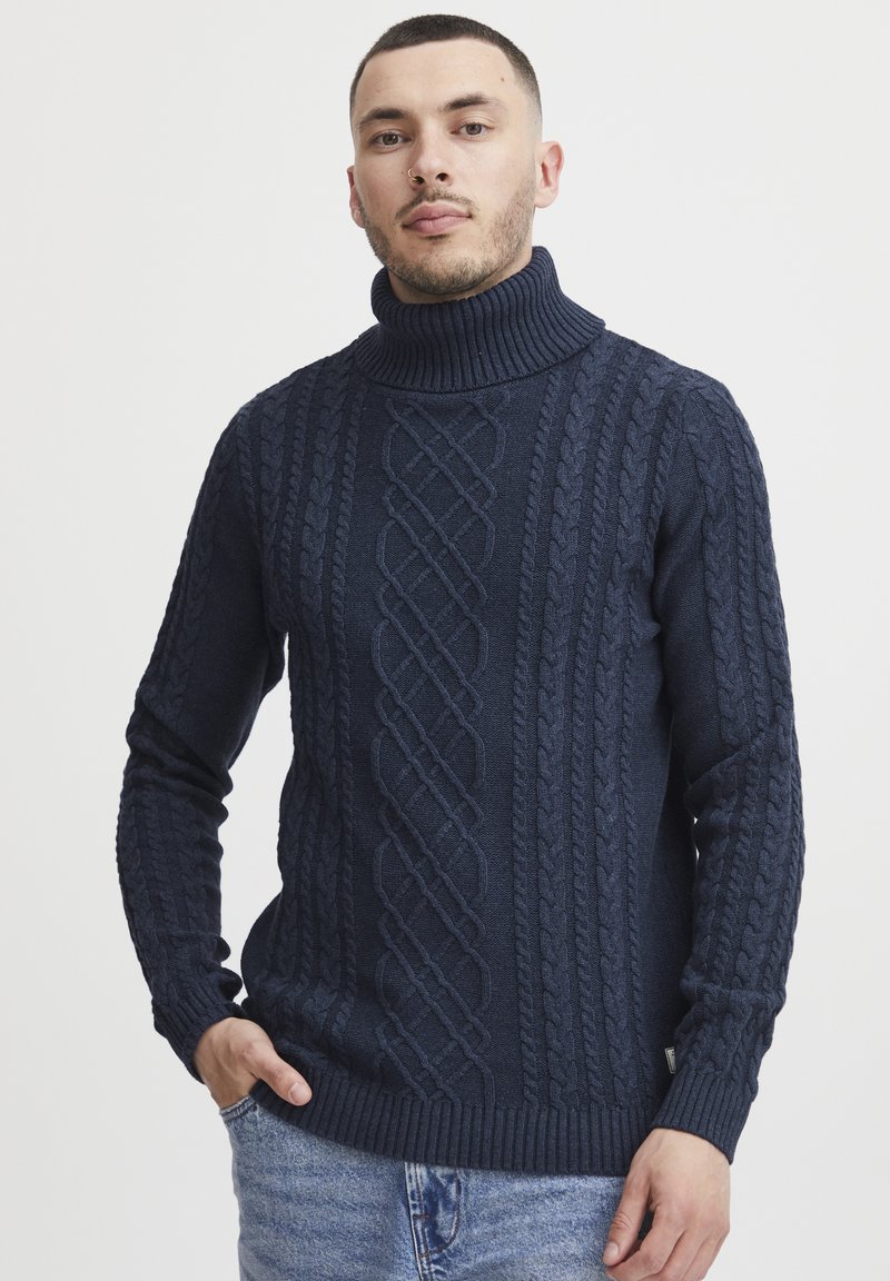 Pull en col roulé en maille bleu marine avec un motif en torsades, des poignets et un ourlet côtelés. Texture douce et coupe ajustée.