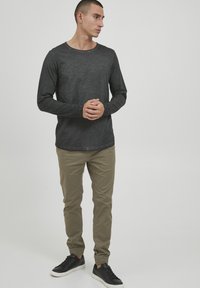 Zwart longsleeve shirt met een ronde hals, gecombineerd met lichtbeige broek en zwarte sneakers. Zacht van textuur, casual ontwerp zonder patronen.
