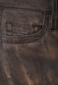 Brun denimtyg med en framficka som har subtila slitna detaljer och sömnadsdetaljer, vilket betonar en robust look.