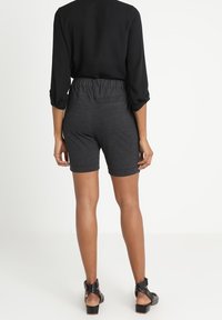 Pantaloni corti grigi elasticizzati con una vita elasticizzata, abbinati a una maglietta nera a maniche lunghe. Tessuto morbido, lunghezza a metà coscia, design casual.