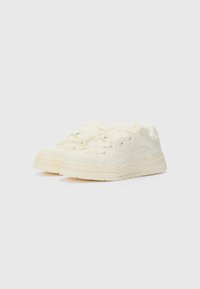 Cream-colored sneakers with a smooth, textured leather upper, lace-up design, padded collar, and thick rubber sole featuring shallow grooves.