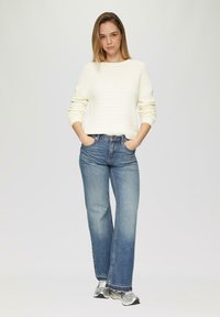 Pull crème clair en maille côtelée avec des manches larges associé à un jean taille haute bleu clair. Les chaussures sont des baskets de sport argentées.