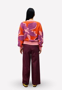 Gebreide trui in oranje, paars en roze met bloemmotieven. Gecombineerd met wijduitlopende bordeauxrode corduroy broek en zwart-gele schoenen.