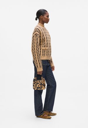 Beige knitted sweater with black patterned accents, high neckline, paired with dark denim jeans, leopard print handbag, and matching shoes.