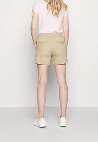 Shorts kaki à coupe droite, avec deux poches arrière et un ourlet net, associés à des baskets blanches.