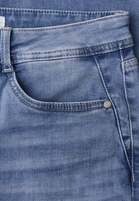 Primer plano del área del bolsillo delantero en unos vaqueros de mezclilla azul con costuras visibles y un remache de metal en el borde del bolsillo.