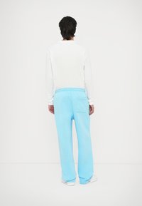 Gaiši zili sporta bikses ar brīvu piegriezumu, elastīgu jostasvietu un aizmugurējo kabatu. Apvienotas ar vienkāršu baltu garām piedurknēm kreklu.