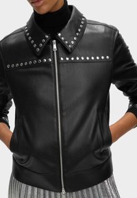 Zwarte leren jas met een drukknoopkraag, zilveren studs aan de voorkant en een voorrits, met zijzakken en geribbelde mouwen.
