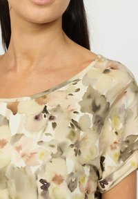 Blomstermønstret topp laget av myk stoff, med vid halslinning, korte rullede ermer, og dempede farger som beige, rosa og grønn.