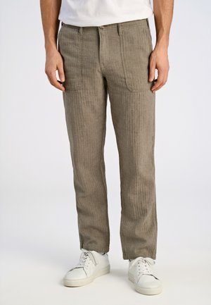 Pantalones ligeros de color beige texturizados con rayas verticales, que cuentan con bolsillos laterales y un corte slim, llevados con zapatillas blancas.