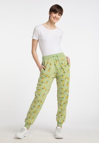 Hellgrüne Sweatpants mit gelben Obstmustern, elastischem Bund mit Kordelzug und Seitentaschen. Kombiniert mit einem weißen T-Shirt und Sneakers.