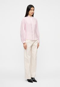 Ροζ ανοιχτόχρωμο μπλουζάκι με μακριά μανίκια και γιακά, με κουμπιά μπροστά και μανίκια με πιέτες. Συνδυάζεται με κρεμ παντελόνι και μαύρα μποτάκια έως τον αστράγαλο.