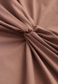 Elastiskt brunt bomullstyg med en knutdesign. Har en slät textur och mjuk drapering som skapar mjuka veck och samlingar.