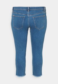 Vaqueros capri de mezclilla azul con dobladillo deshilachado, dos bolsillos traseros y sutiles acentos de costura naranja. Textura suave, diseño ajustado.