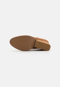 Bottine en daim marron avec un talon bloc et un bout arrondi. La semelle présente un motif de grip texturé et est marquée "TOMS."